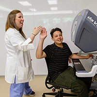 A female doctor high-fiving a young male patient as he sits at a computer.
