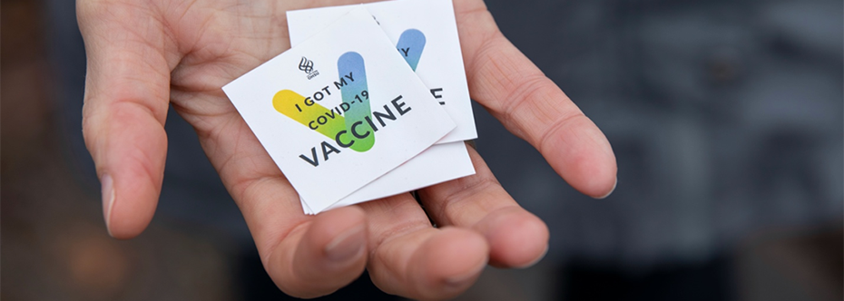 A hand holding a stack of "I got my COVID-19 Vaccine" stickers
