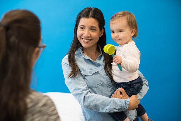 Photo of a woman standing holding a toddler who has a toy