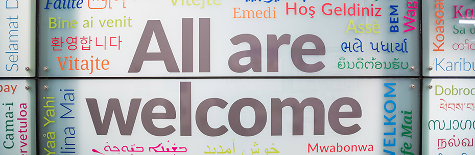Photo of a wall painted with the words "All are welcome" in several different languages.