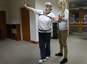 A female provider stands behind an older female patient as the patient attempts to stay balanced while walking a straight line.