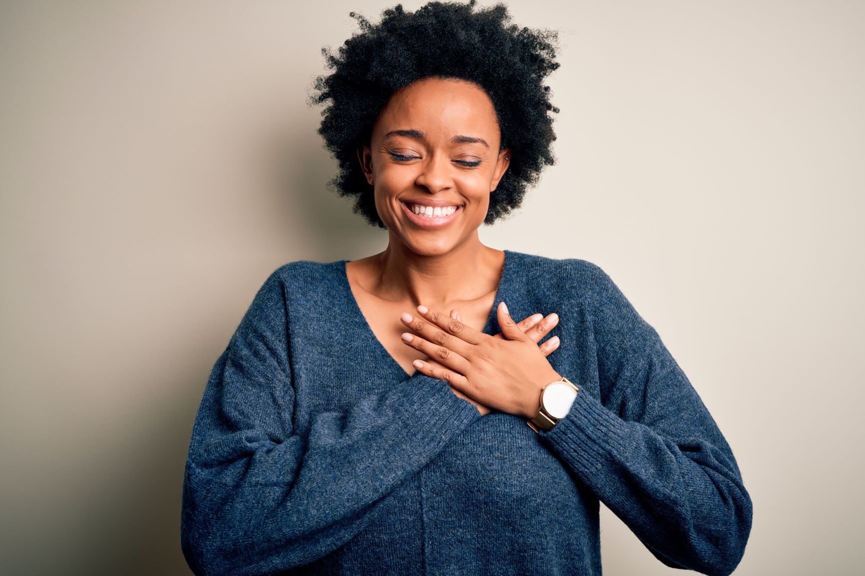 Woman in sweater smiles big with hands over heart.