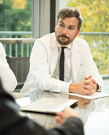 A doctor sitting at a conference room table listening during a meeting.