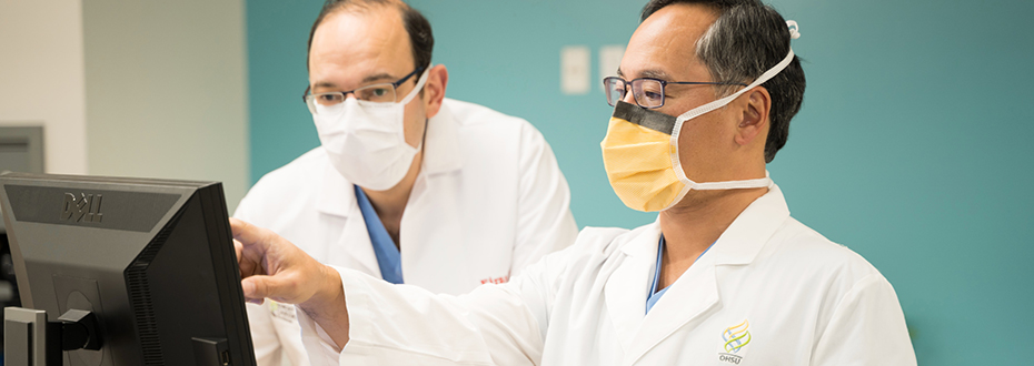 Two male doctors wearing PPE facemasks looking at a computer screen.