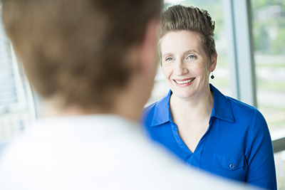 A provider with back to the camera in the foreground, speaks with a smiling patient.