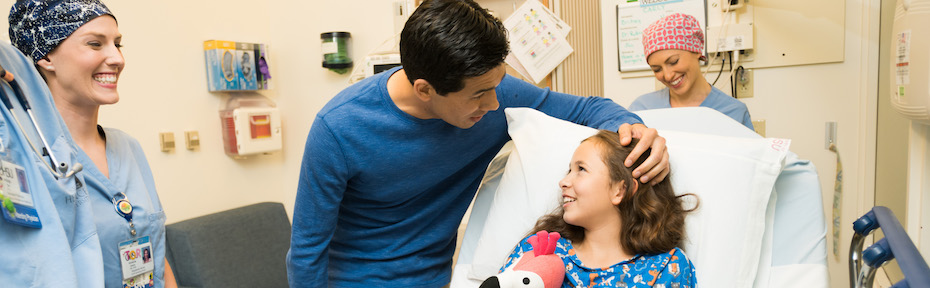 A child in a hospital bed, with a parent and healthcare providers standing nearby