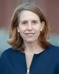 Headshot of Allison Lindauer, wearing a navy blue jacket, against a blurred brick background