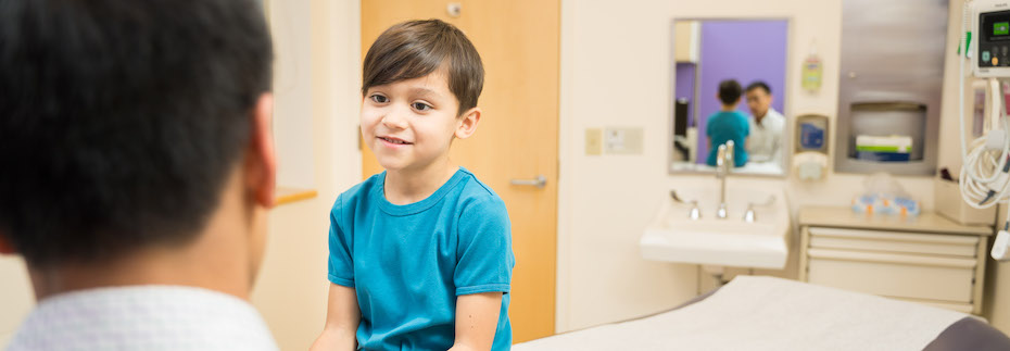 Photo of a child sitting on an exam table talking with a healthcare provider