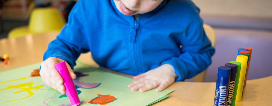Photo of a child wearing a blue sweater holding a paint stick and coloring on green paper
