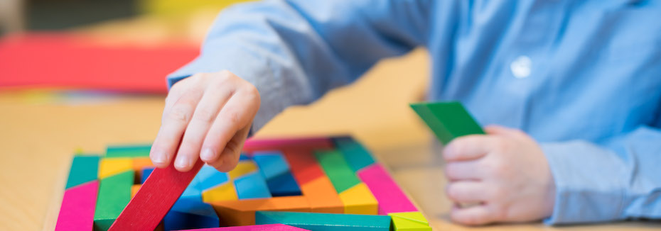 Photo of a child's hands, the child is holding colorful blocks and building a design on a table