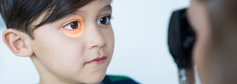 A young boy having his eye examined by a provider who is shining a light into it.