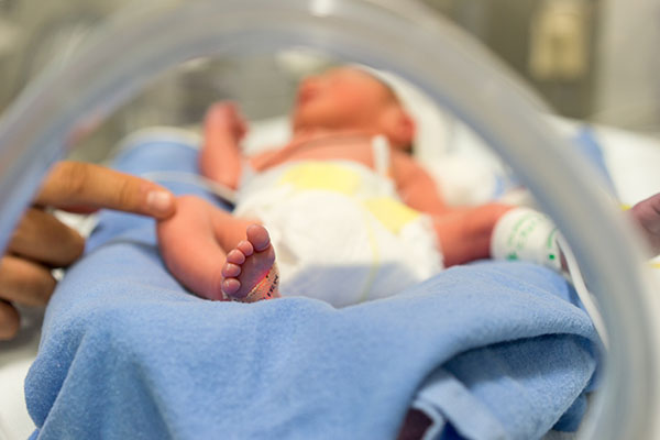 A photo of a baby in Doernbecher Children's Hospital's NICU with a provider reaching in and touching its knee with a finger.