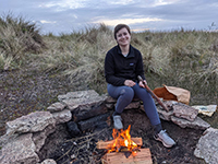 Dr. Annalise Van Meurs siting in front of a campfire smiling.