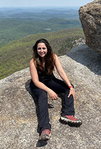 A woman sitting on top of a mountain smiling while on a hike.