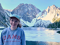 A woman smiling with a frozen lake and snowy mountains behind her.