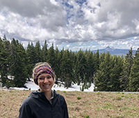 A woman smiling while on a hike with trees behind her and snow on the ground.