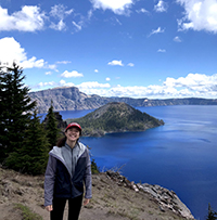 A woman smiling while on a hike with Crater Lake behind her.