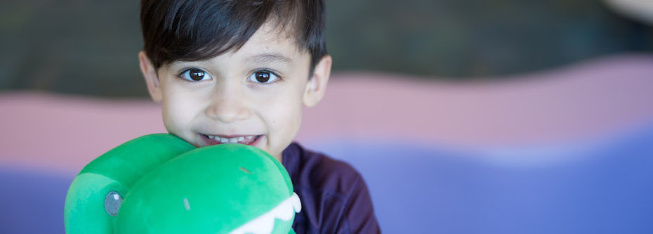 Photo of a smiling child holding a stuffed green dinosaur toy