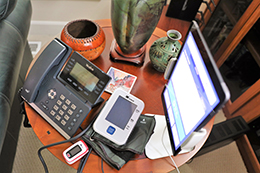 A photo of a side table that has a telephone, a propped up tablet computer and some miscellaneous items including a few vases.
