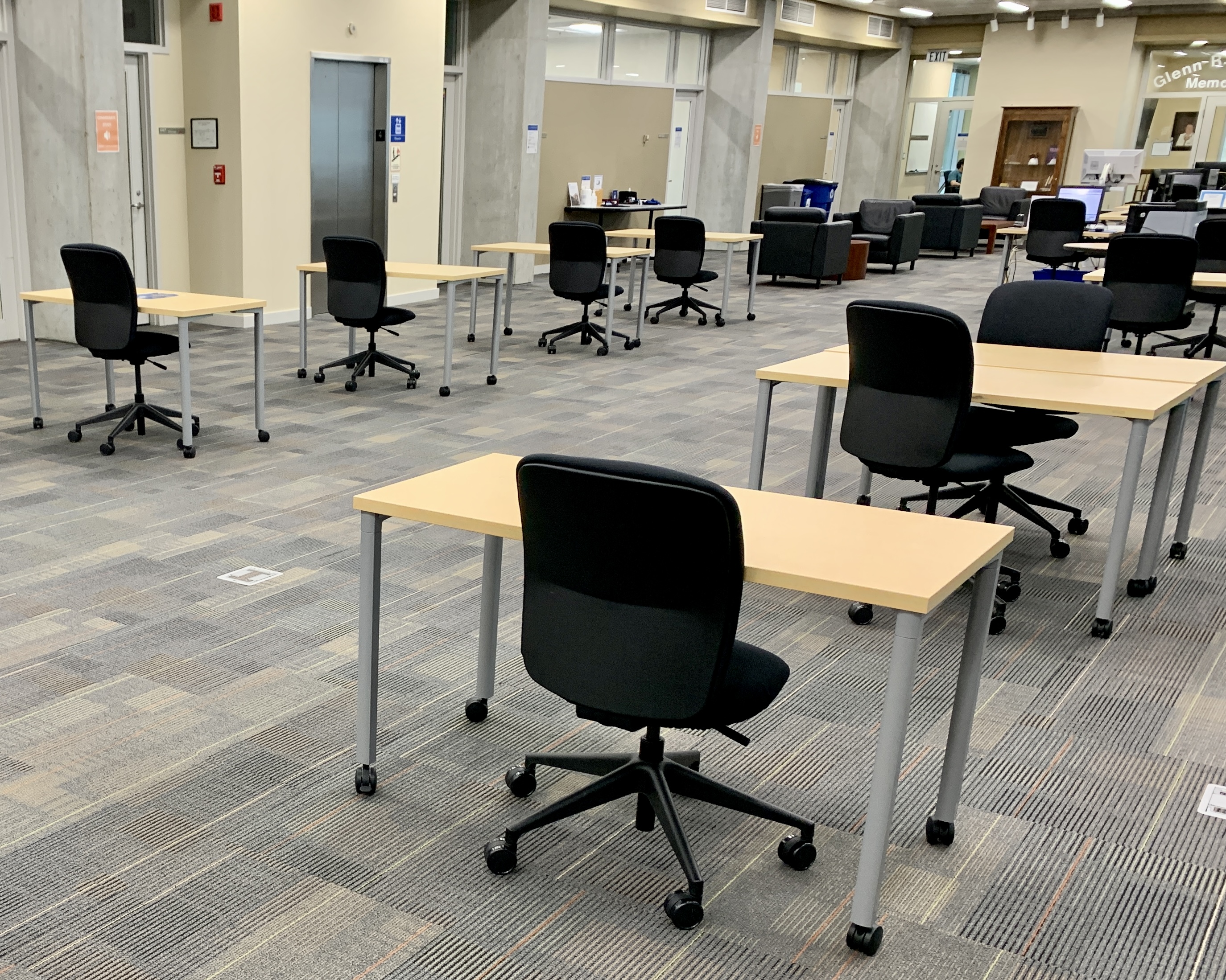 An open library sapce depicts rows of individual desks on wheels with black office chairs on wheels sitting at each. 