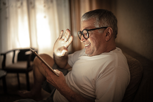 Older gentleman waving to virtual class members via an ipad