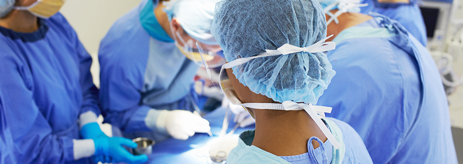 A group of five healthcare providers, all masked and in scrubs, performing a heart surgery on a fully-covered patient.