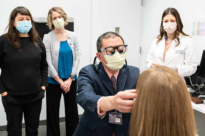 Dr. John Ng examines a patient with colleagues in the background.