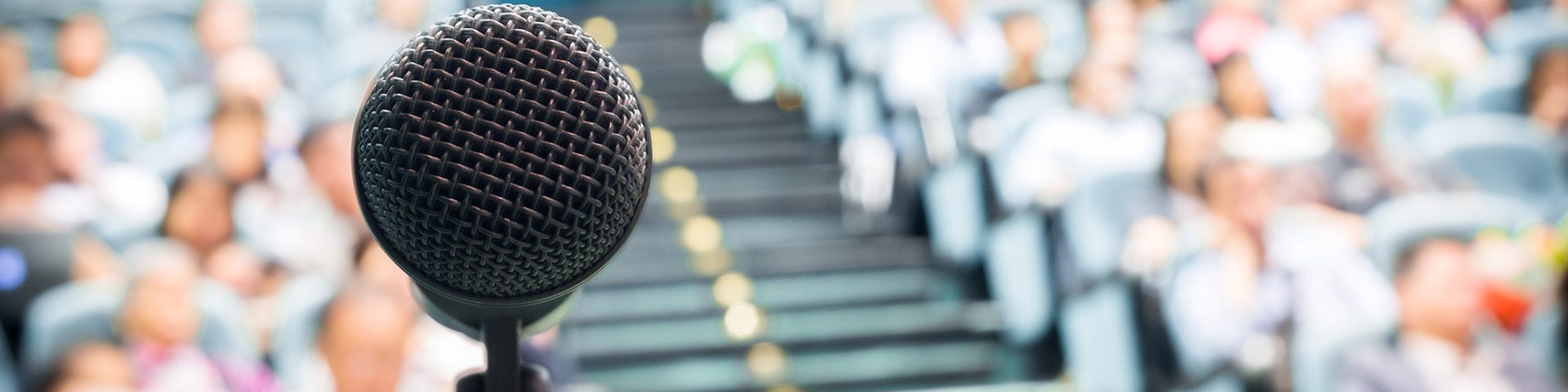 Microphone in front of an auditorium of people. Image courtesy of Getty Images