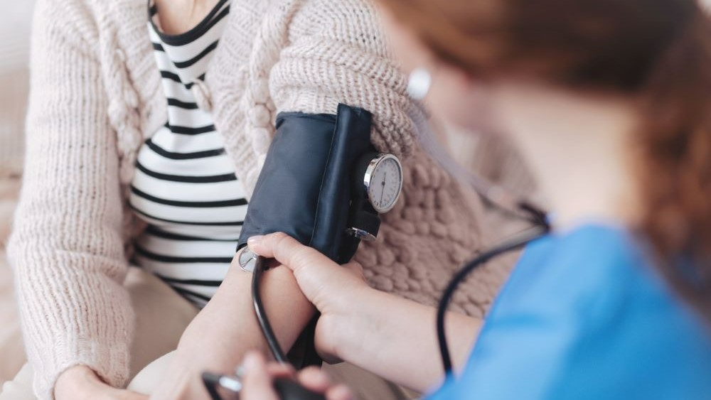 Provider takes blood pressure of a woman in a sweater