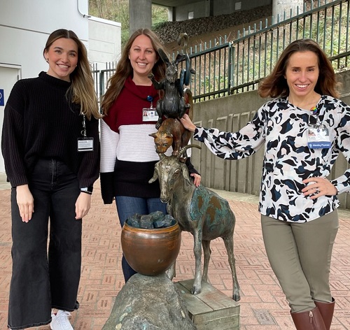Three women smiling around a statue of animals.