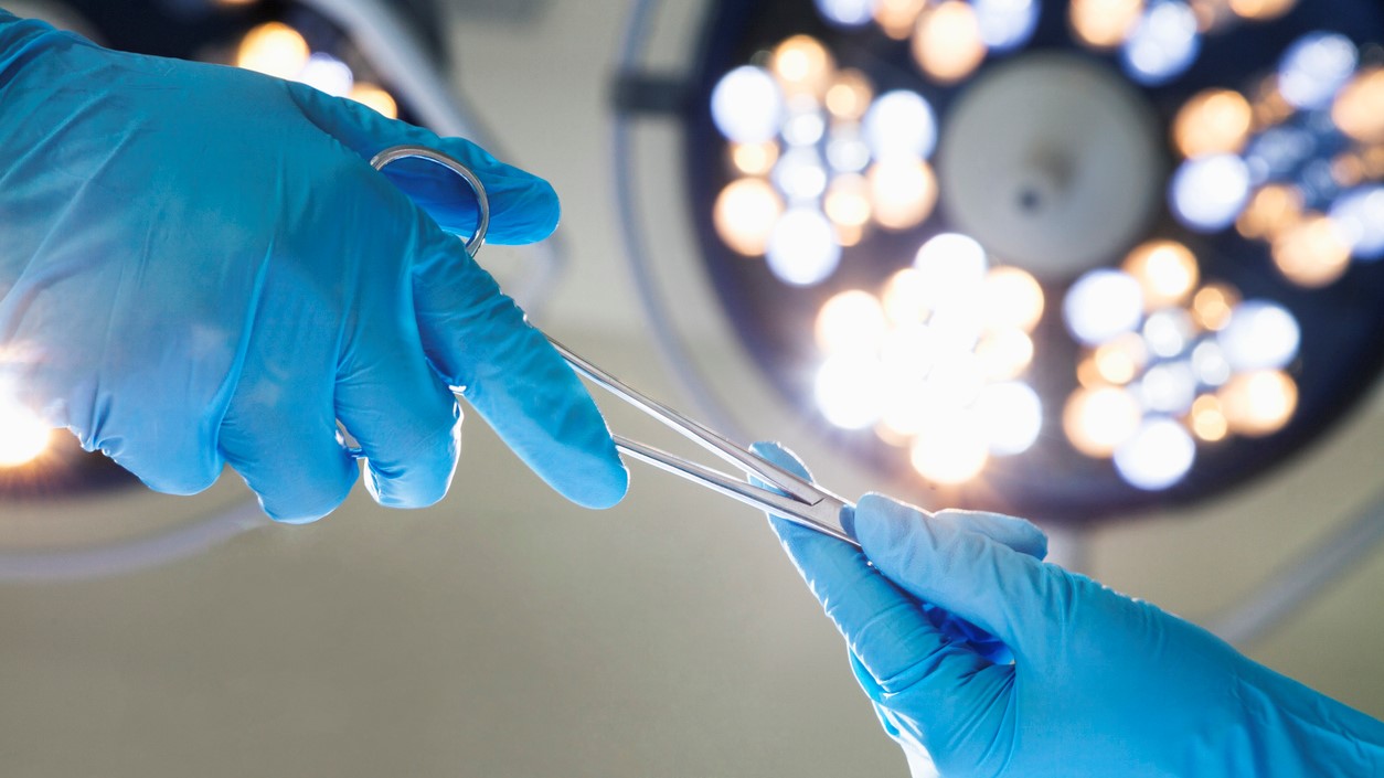 Two surgeons exchange a tool under surgical lights