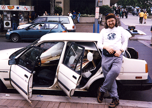 David Oaks smiles with a white car full of protest signs