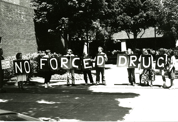 Black and white photograph of protesters with "No Forced Drugs" banner