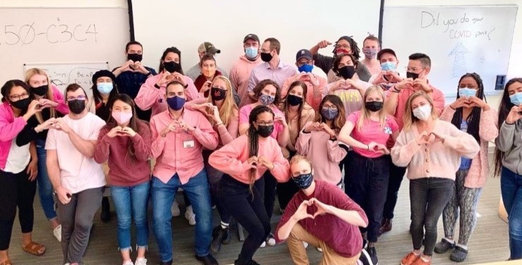 Students standing together wearing pink and forming a heart with their hands.