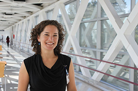 A woman smiling as she stands in the OHSU skybridge to the Portland VA Hospital.