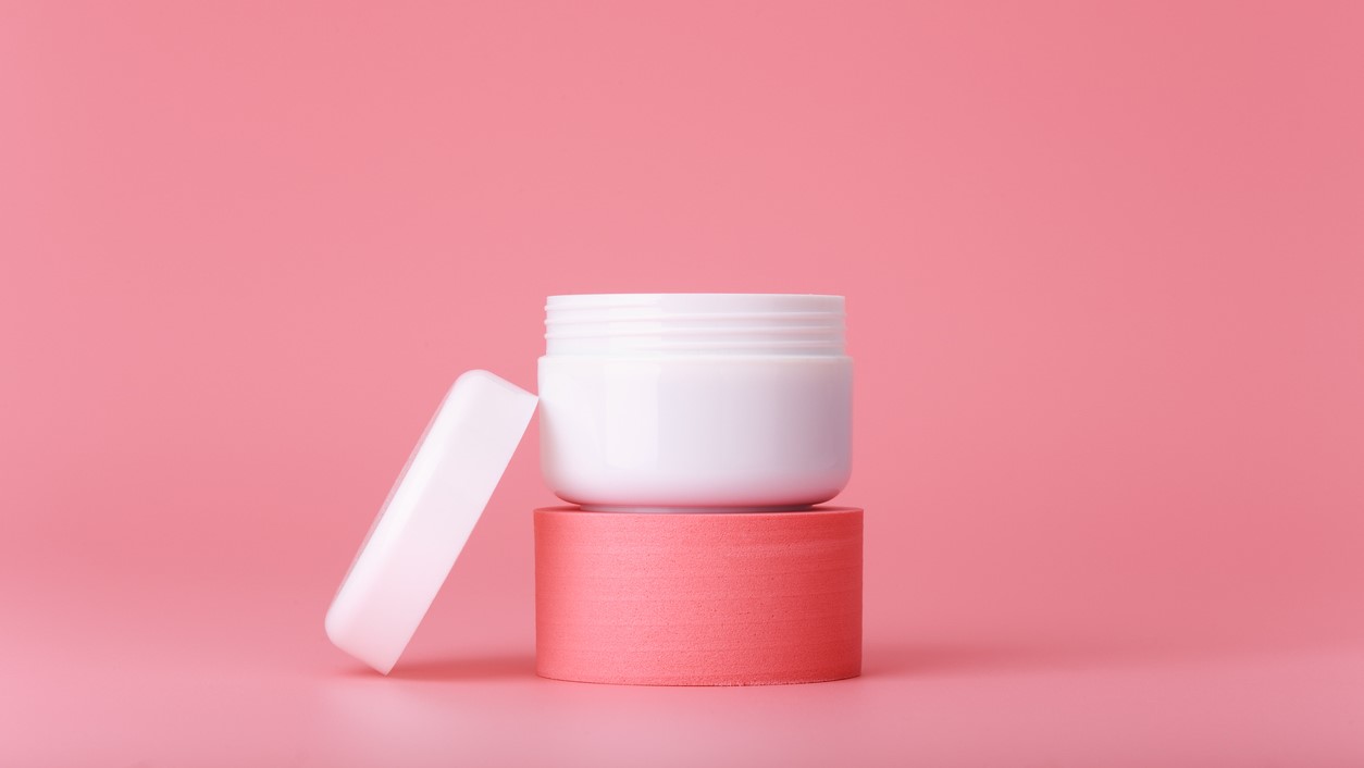 Container of moisturizer sits on stand on pink background