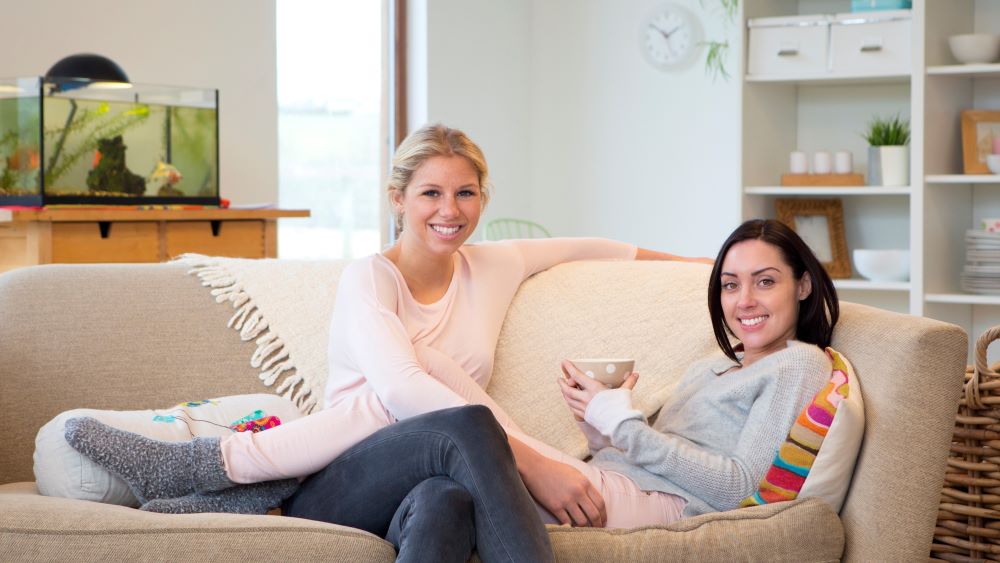 Two smiling women sit on cozy couch