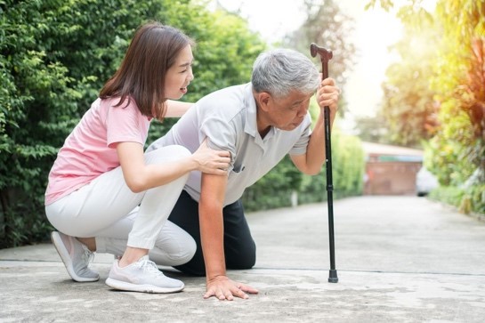 A young woman assisting an elderly man up from a fall.