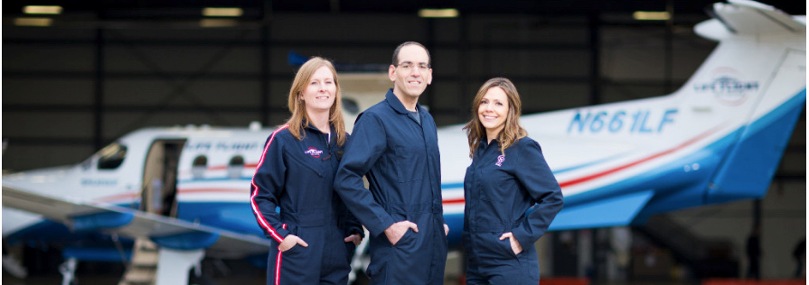 Three members of the Trama Team standing in front of a transport plane.