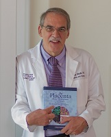 Dr. Myatt is wearing a white lab coat and holding a placenta textbook. 