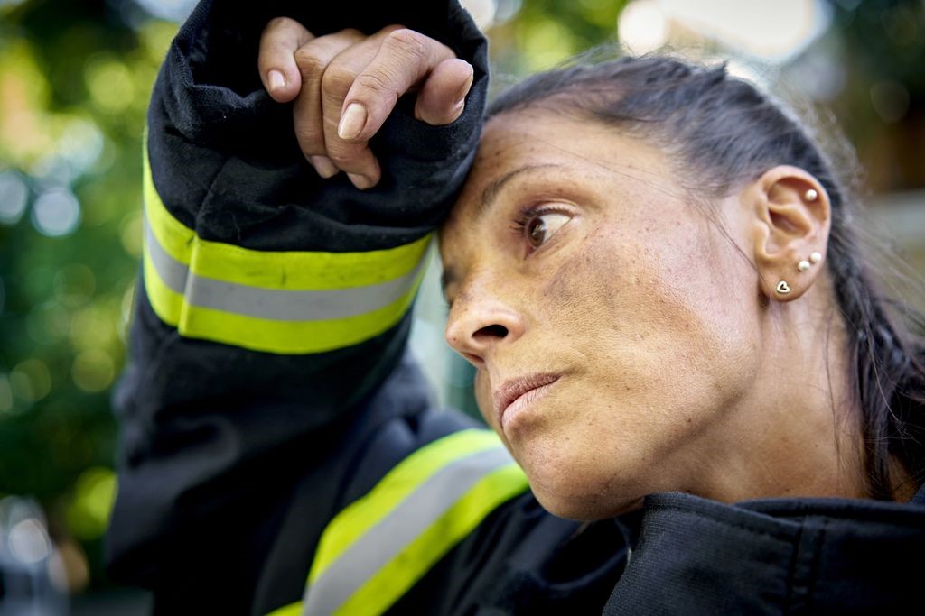 A female firefighter pauses to wipe the sweat from her brow.