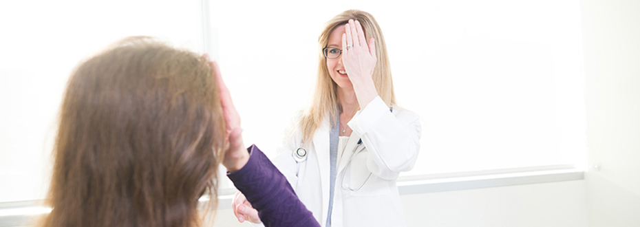 Dr. Elena Varlamov in a white lab coat with a patient. Both covering one eye