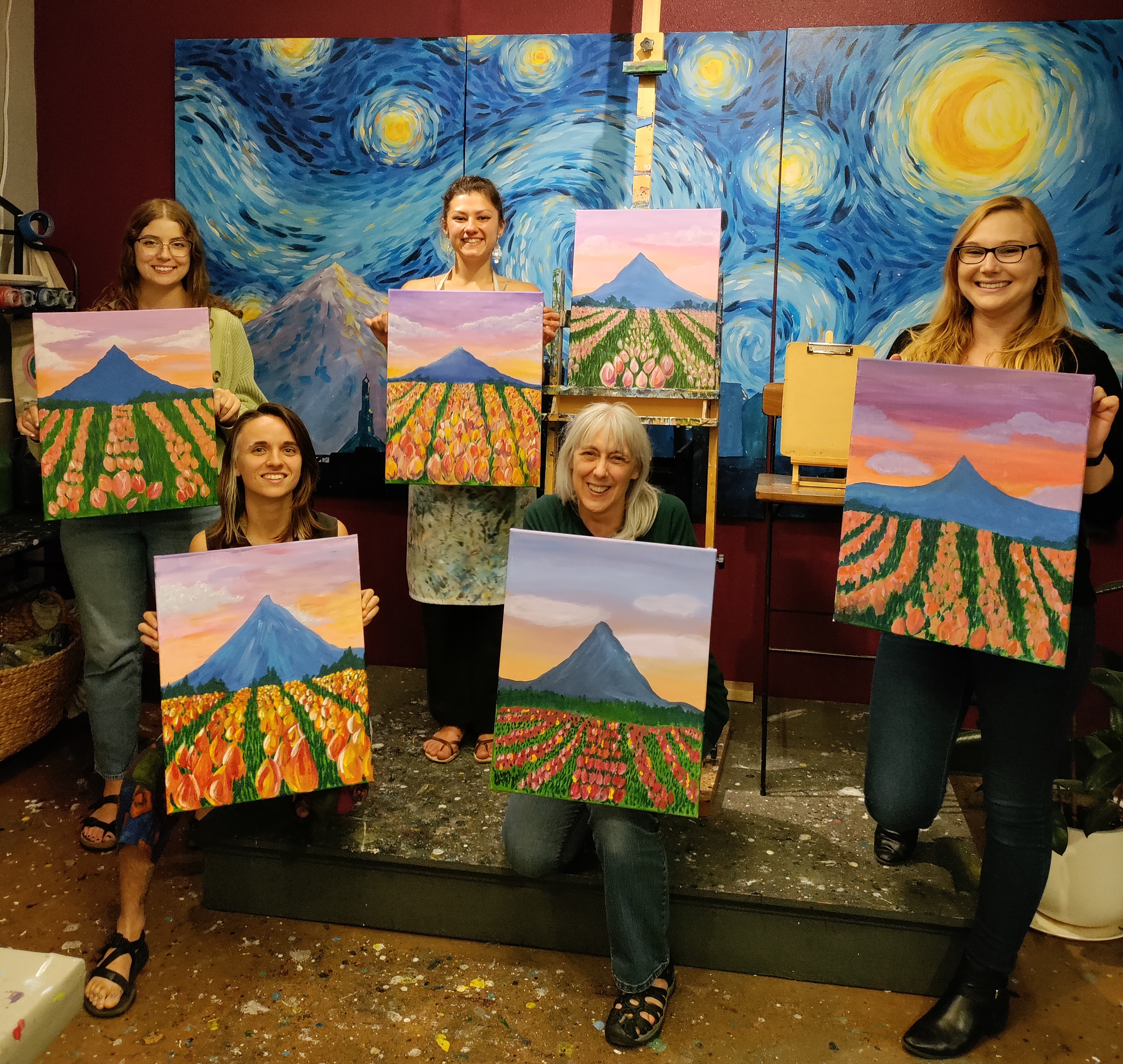 Members of the lab holding their paintings of mount hood and a field of tulips