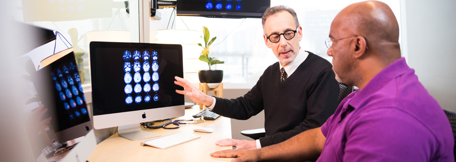 Dr. Jeffrey Kaye talking to a colleague in front of two computer screens displaying brain imaging results