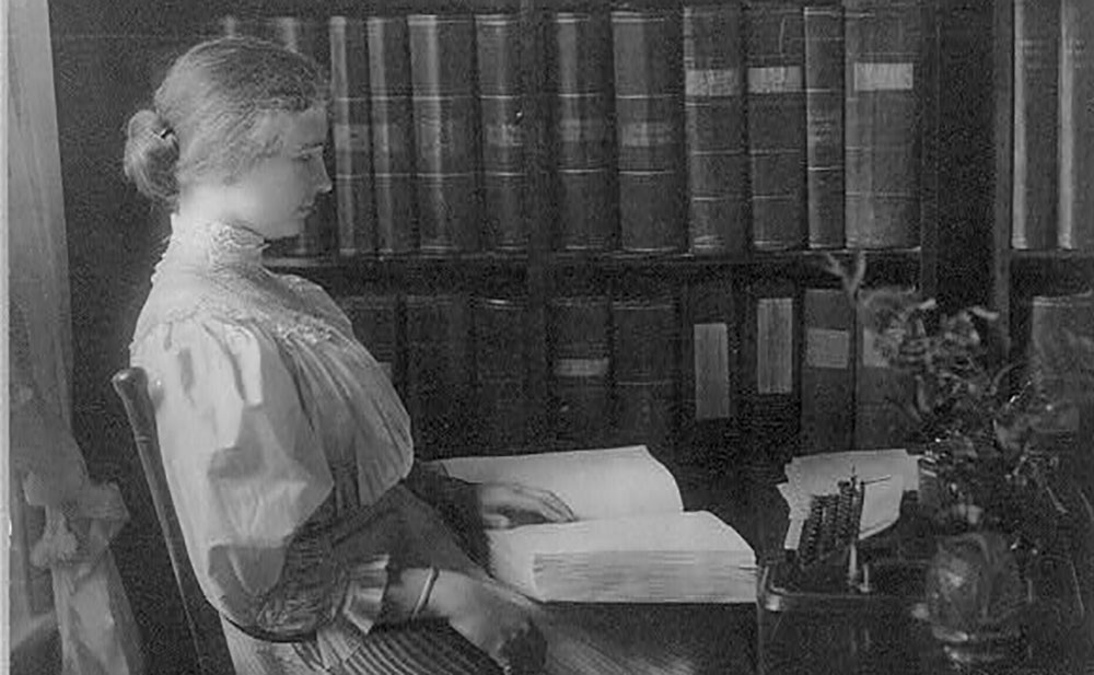 Helen Keller sits in a chair reading