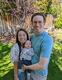 A man and a woman holding their baby smiling in a backyard.