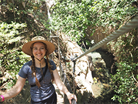 A woman smiling while standing on a rope bridge.