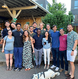 A group of residents pose together at an outdoor area in Portland with a dog in front.