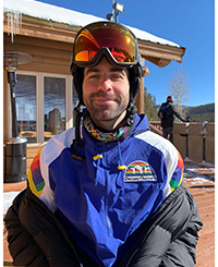 A man in ski gear smiling outside on a sunny day.