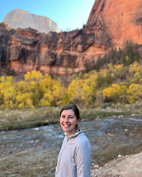A woman smiling standing in front of a river in a canyon.